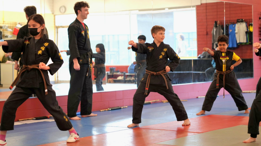 A group of youth students in black uniforms practicing punch techniques during a structured martial arts class at Yuen's Family Martial Arts in Coquitlam.