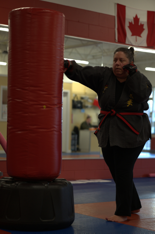 A woman practicing heavy bag strikes during an adult martial arts fitness class at Yuen's Family Martial Arts.