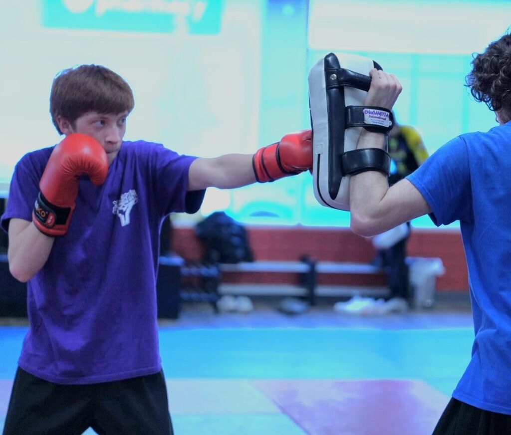 Two young men practicing boxing combinations with focus mitts and strike pads at a martial arts gym in Coquitlam.