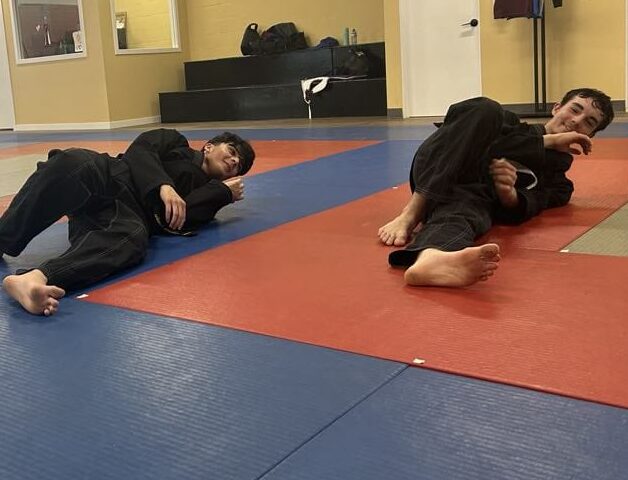 Youth students in white and black uniforms learning foundational grappling and ground defense drills on the mats at Yuen's Family Martial Arts in Coquitlam.
